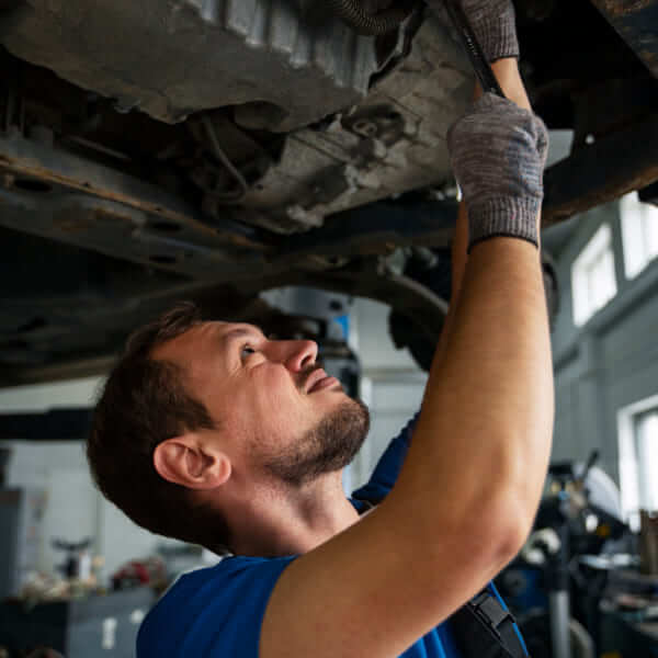 Un mécanicien avec des gants utilisant une clé pour réparer le dessous d'un véhicule dans un atelier de réparation automobile.