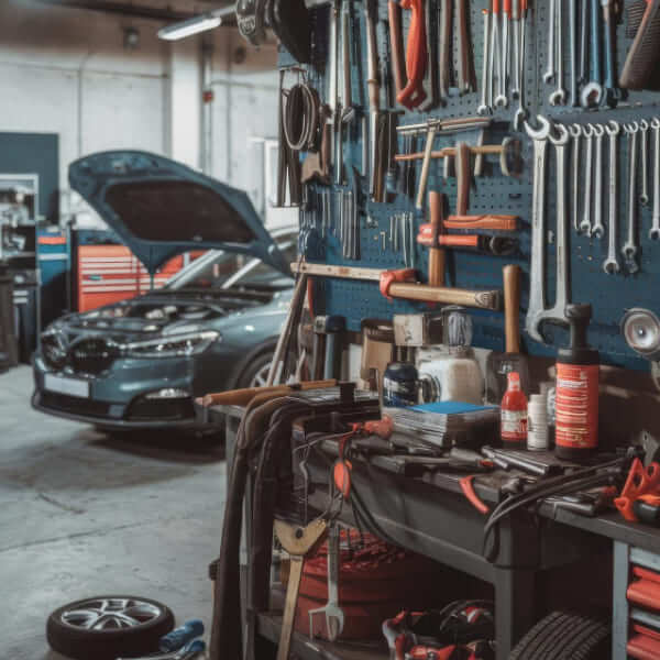 A wall-mounted blue pegboard filled with neatly arranged wrenches and hand tools next to a workbench, with a car with its hood open in the background.