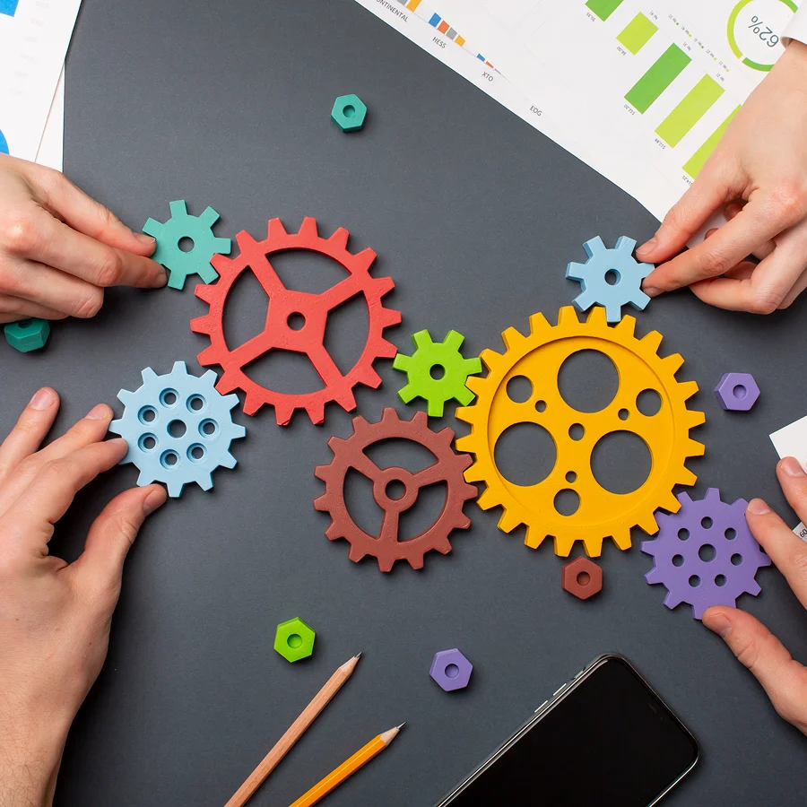 Transformez vos projets en atouts durables grâce à une gestion des actifs stratégique : la promesse du Groupe AVA 1 Des mains tenant des engrenages colorés sur une table, symbolisant la gestion des actifs.