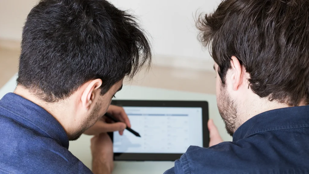 Révolutionnez vos projets avec une maintenance intelligente : l'approche puissante du Groupe AVA 7 Deux hommes examinant un ordinateur tablette, discutant de la maintenance intelligente.