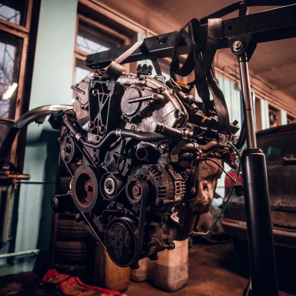 Moteur WEG : performance et efficacité pour l’industrie 1 Moteur de voiture suspendu par une grue d'atelier dans un garage de réparation automobile.